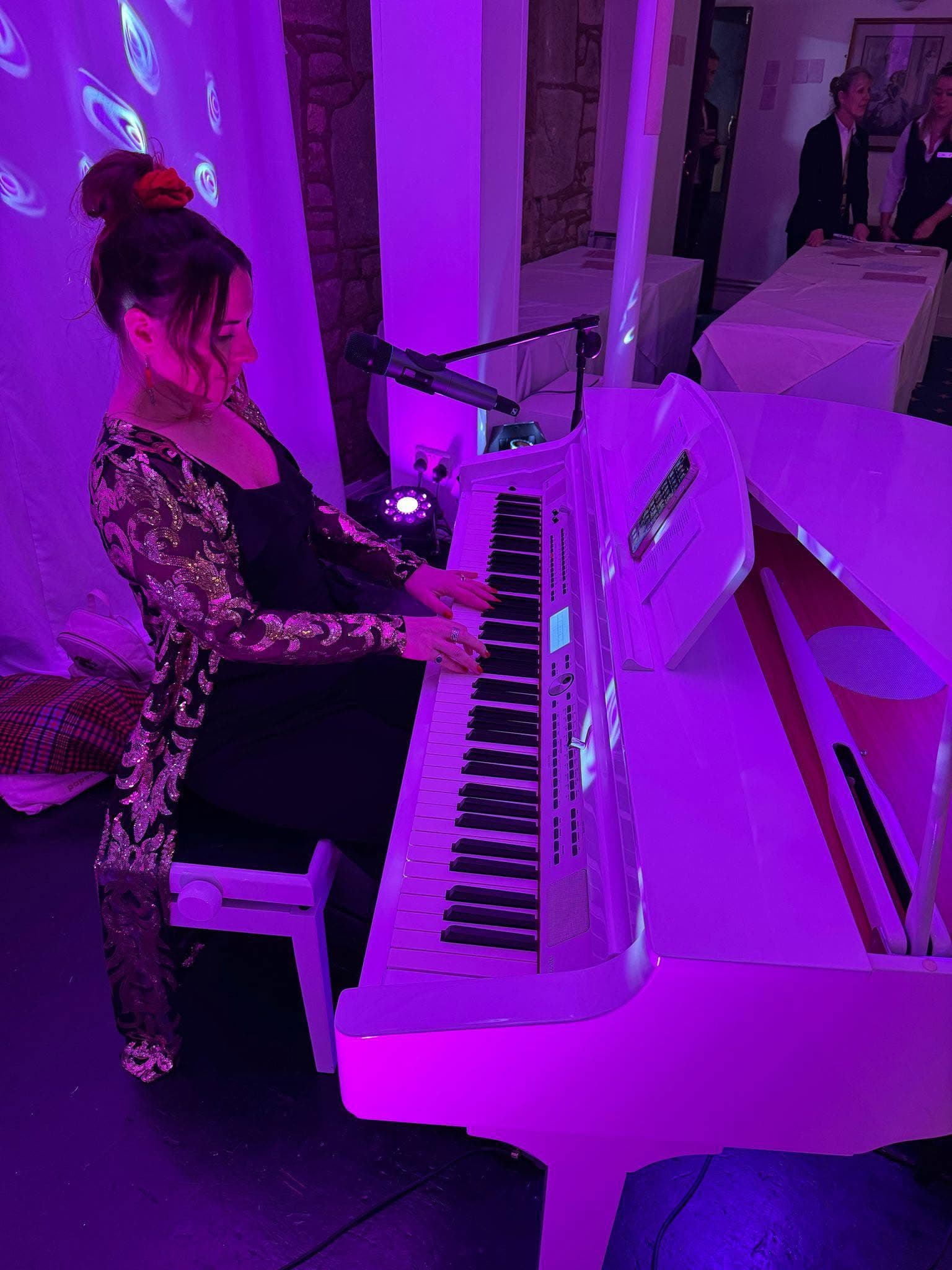A pianist playing the white piano under purple light